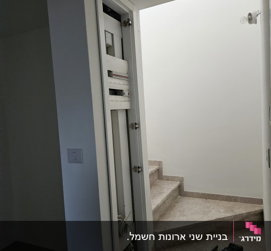מקדחה מונחת על מדרגות ליד ארון חשמל פתוח